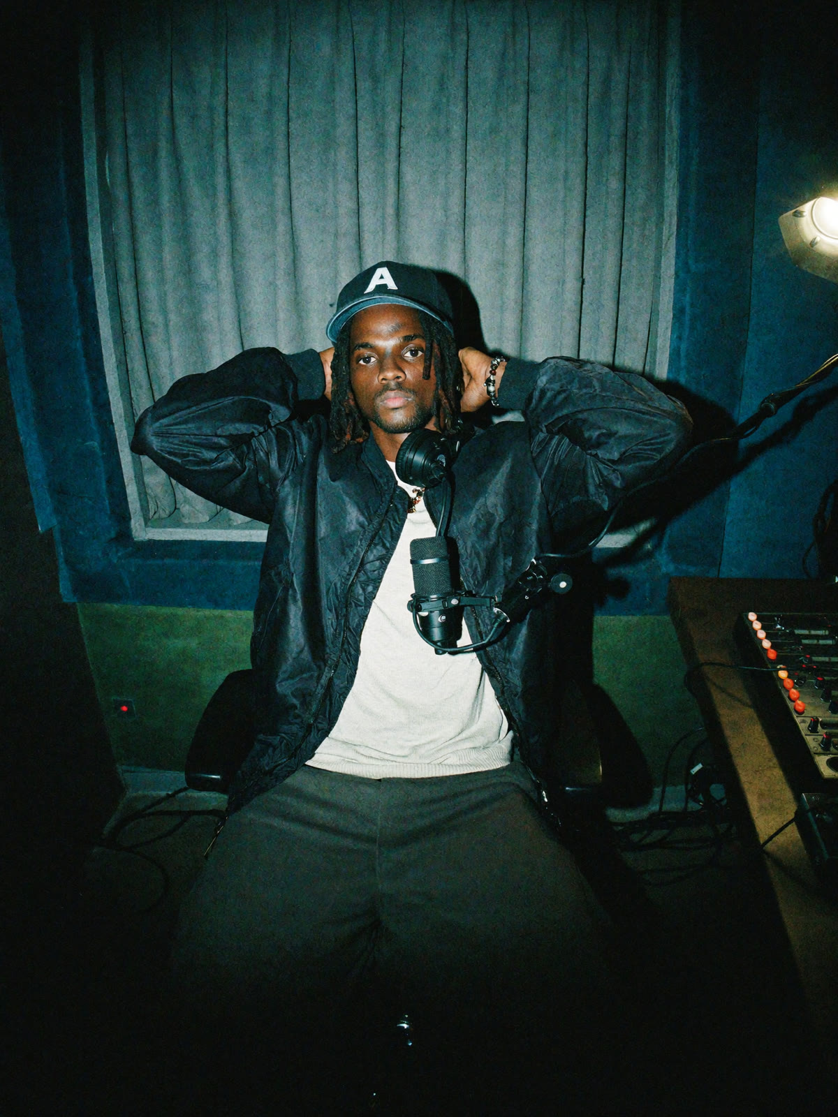 Azu in the studio, hands behind his head, headphones around his neck